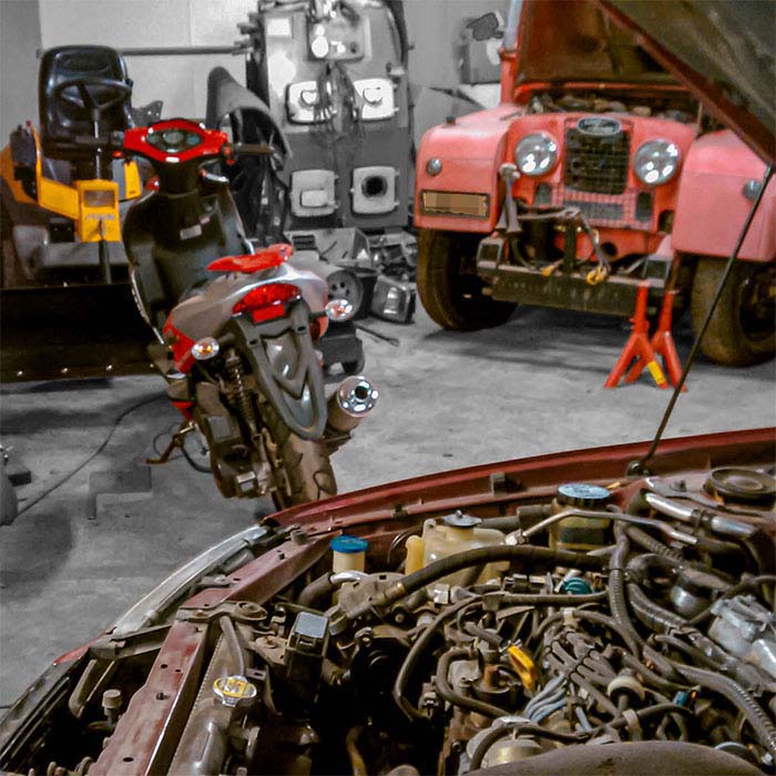 Hallilla on korjattavana museoauto, ruohonleikkuri, skootteri, ja henkilöautosta on konepelti auki.